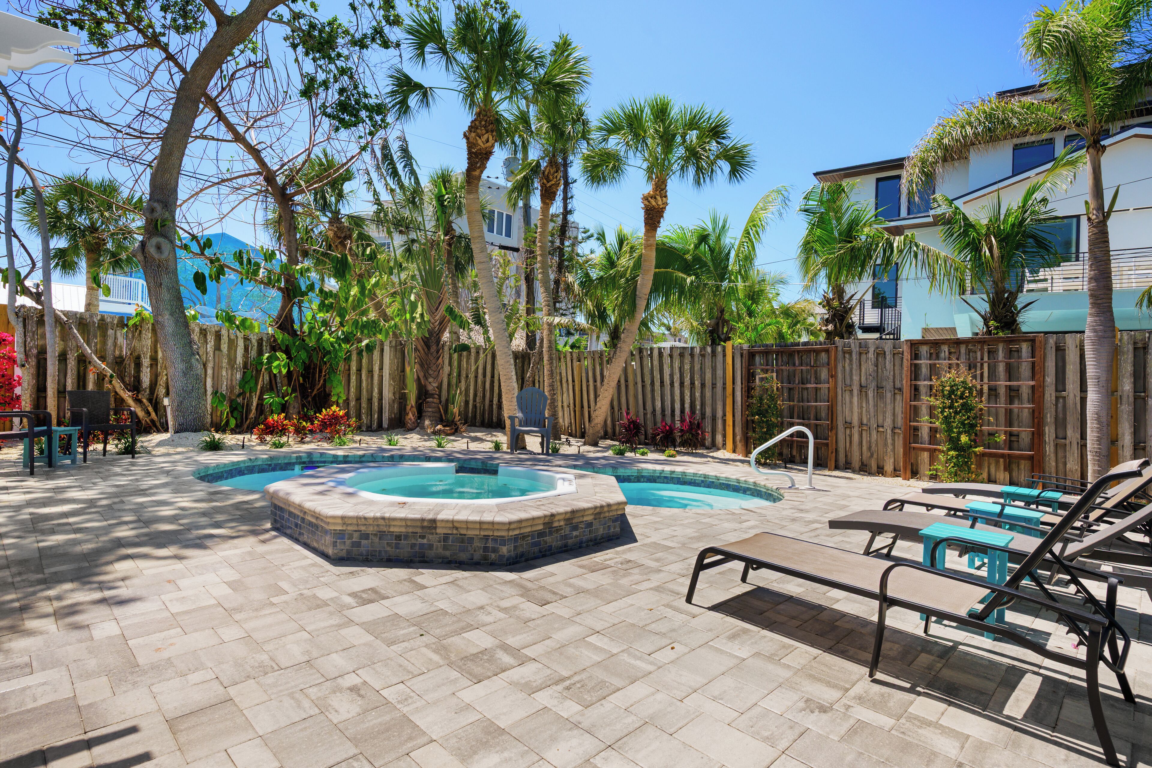 A backyard with a hot tub, lounge chairs, and a wooden fence.