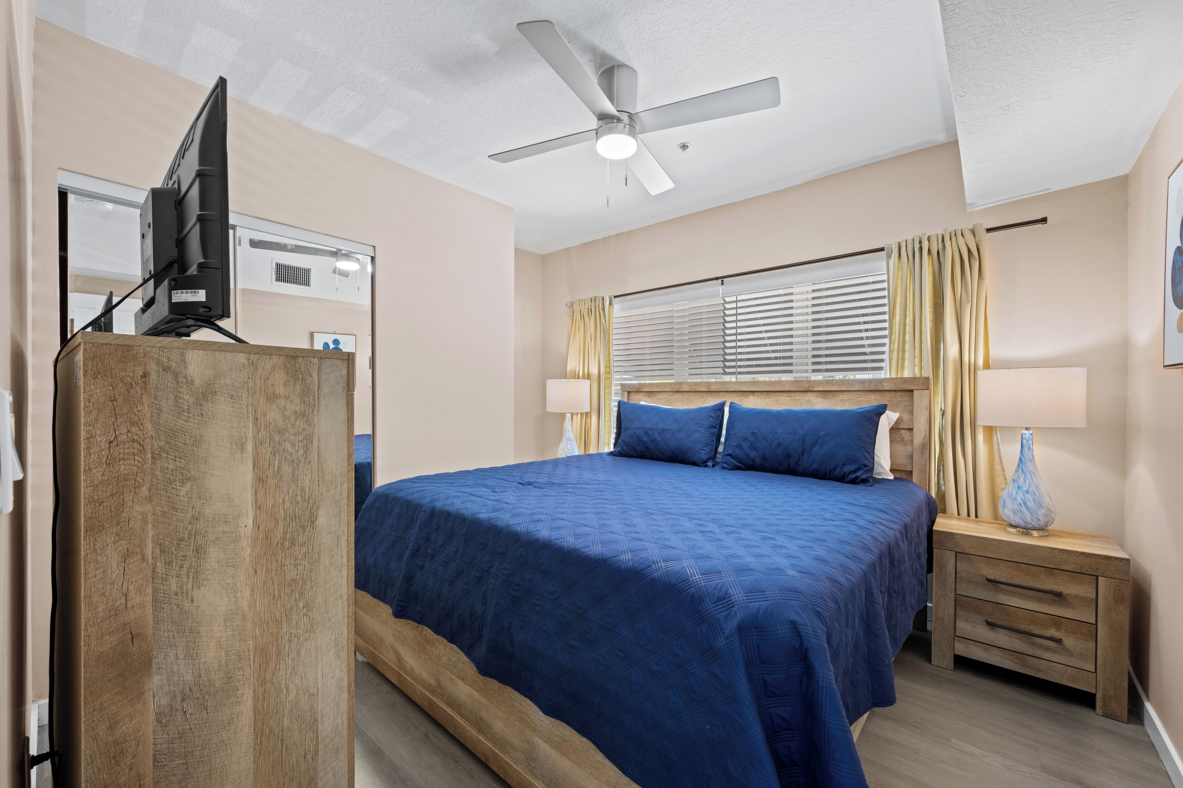 A bedroom with a bed, bedside table, lamp, and ceiling fan.