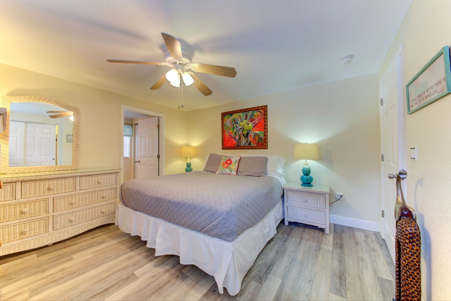 A bedroom with a bed, nightstands, a ceiling fan, a mirror, and a painting.