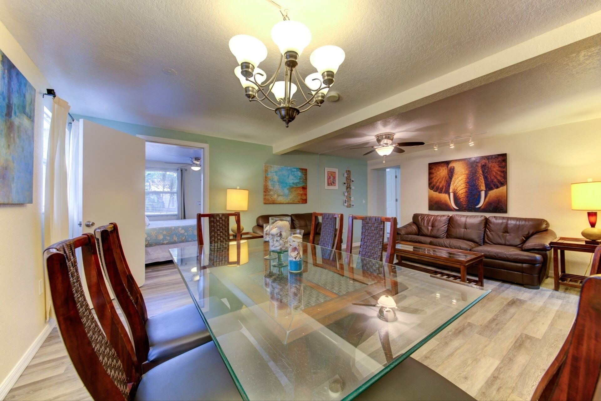 A spacious living area with a glass-top dining table, leather sofa, and a chandelier.