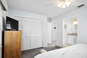 A bedroom with a bed, a wardrobe, a television on a wooden cabinet, and a ceiling fan.