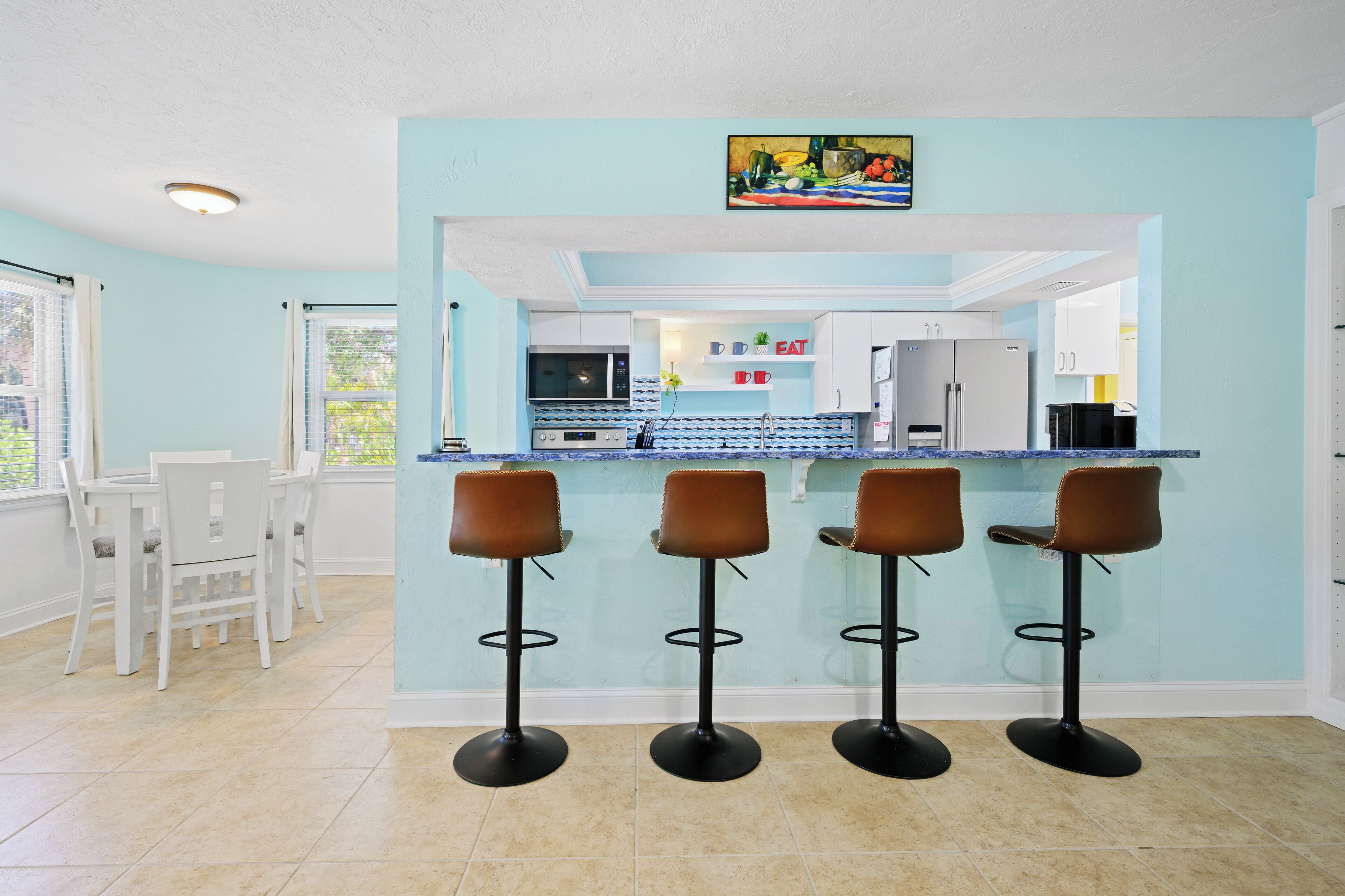 A modern kitchen with a bar area, white cabinets, and a blue backsplash.