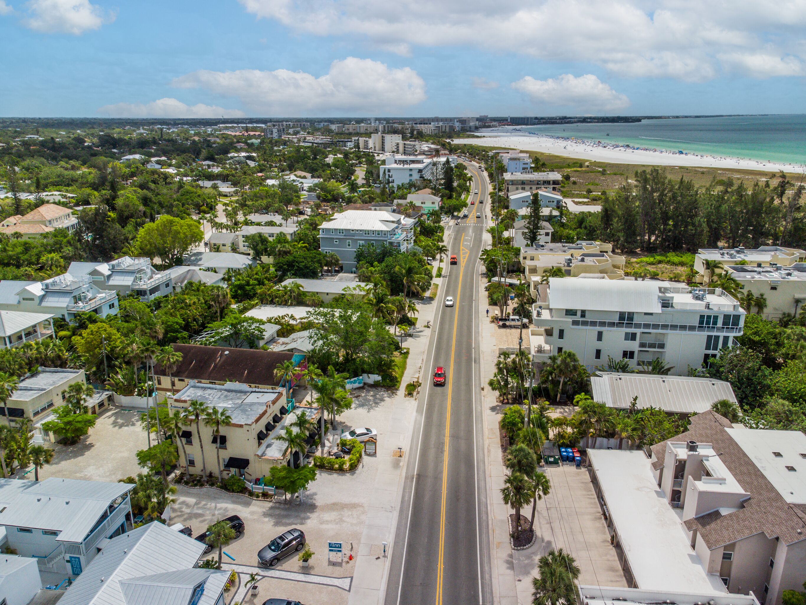 An aerial view of a coastal town with a main road, beachfront, and residential buildings.