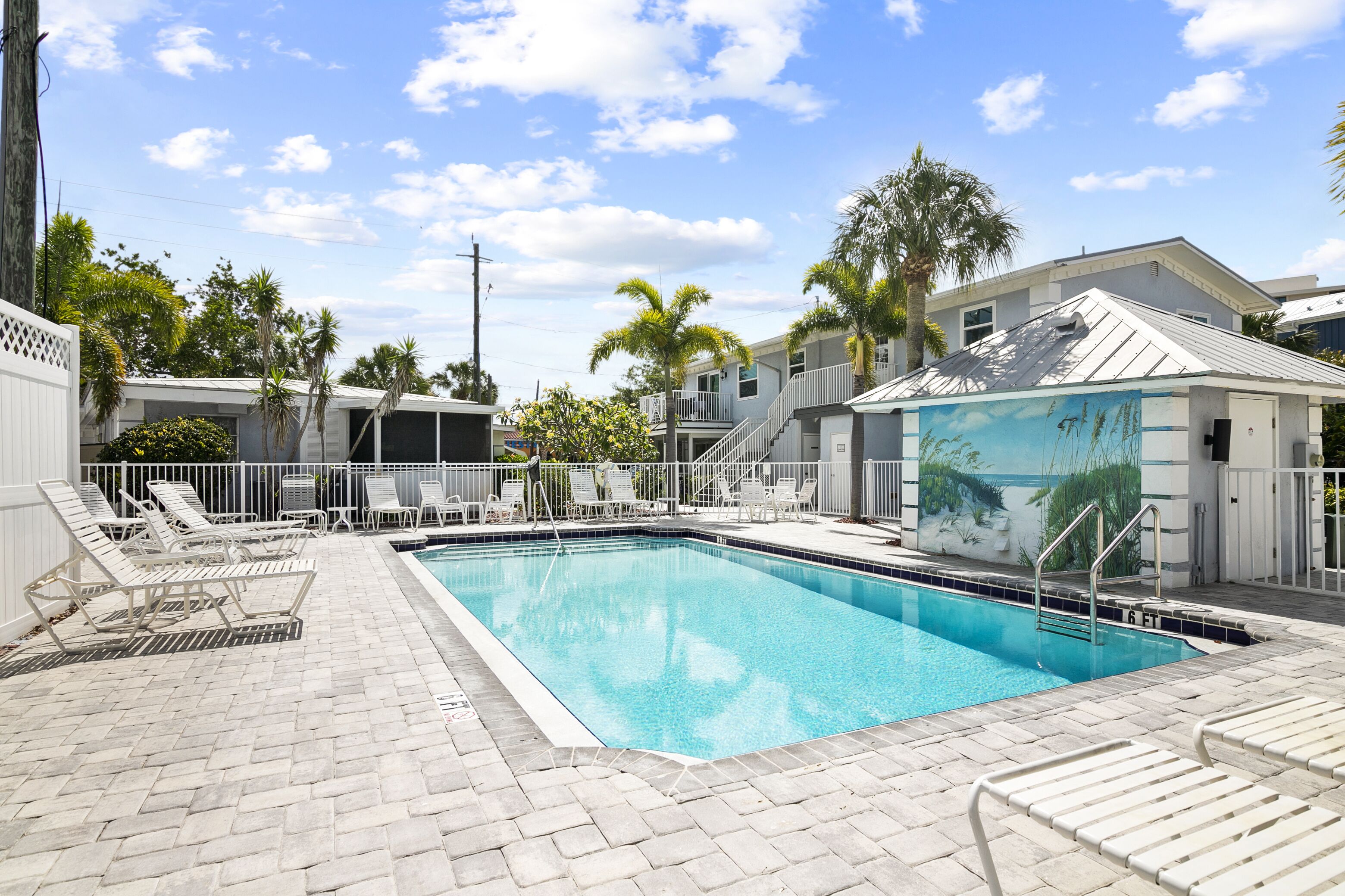 A swimming pool with lounge chairs, palm trees, and a building with a mural.