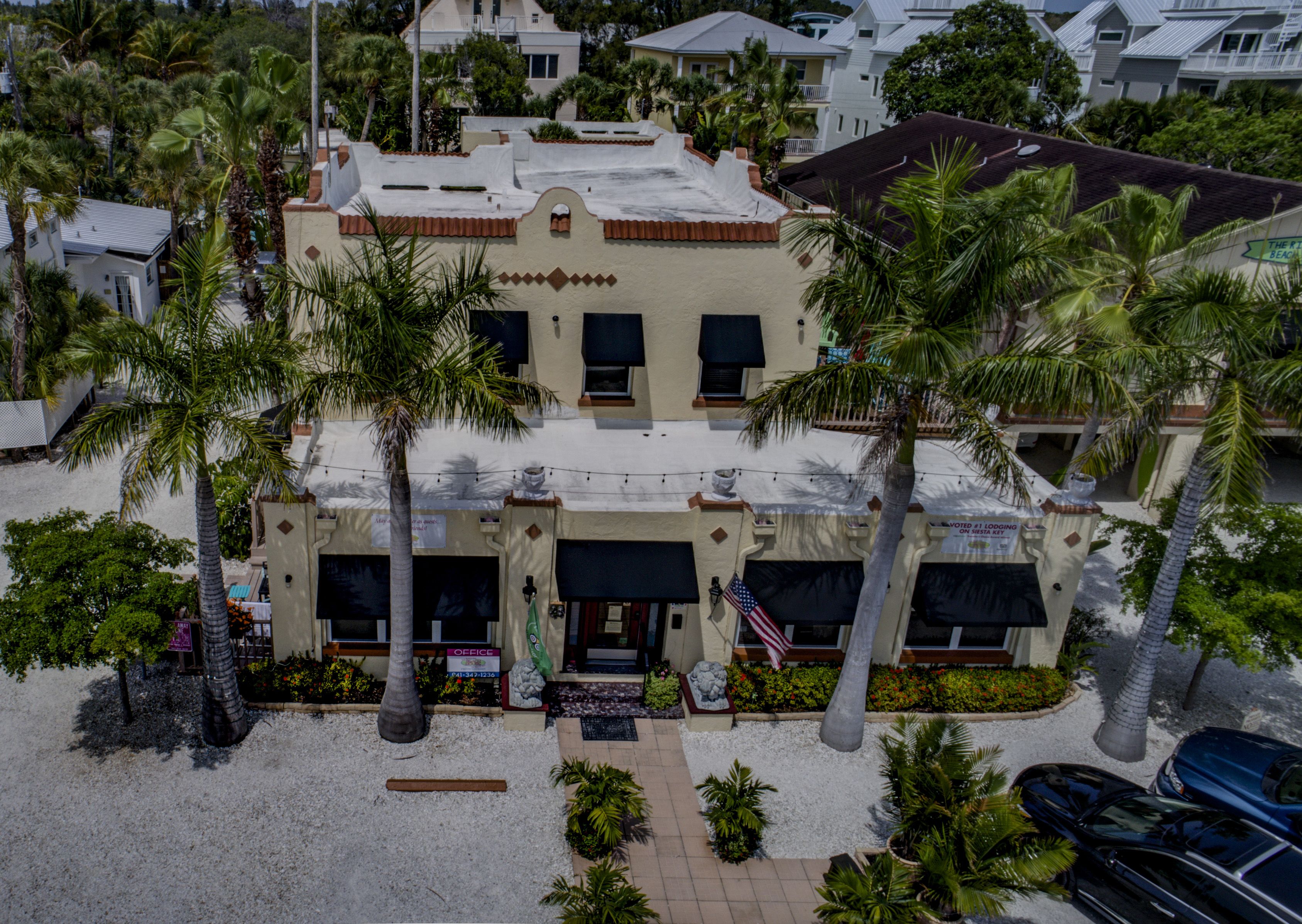 A two-story building with a flat roof, surrounded by palm trees.
