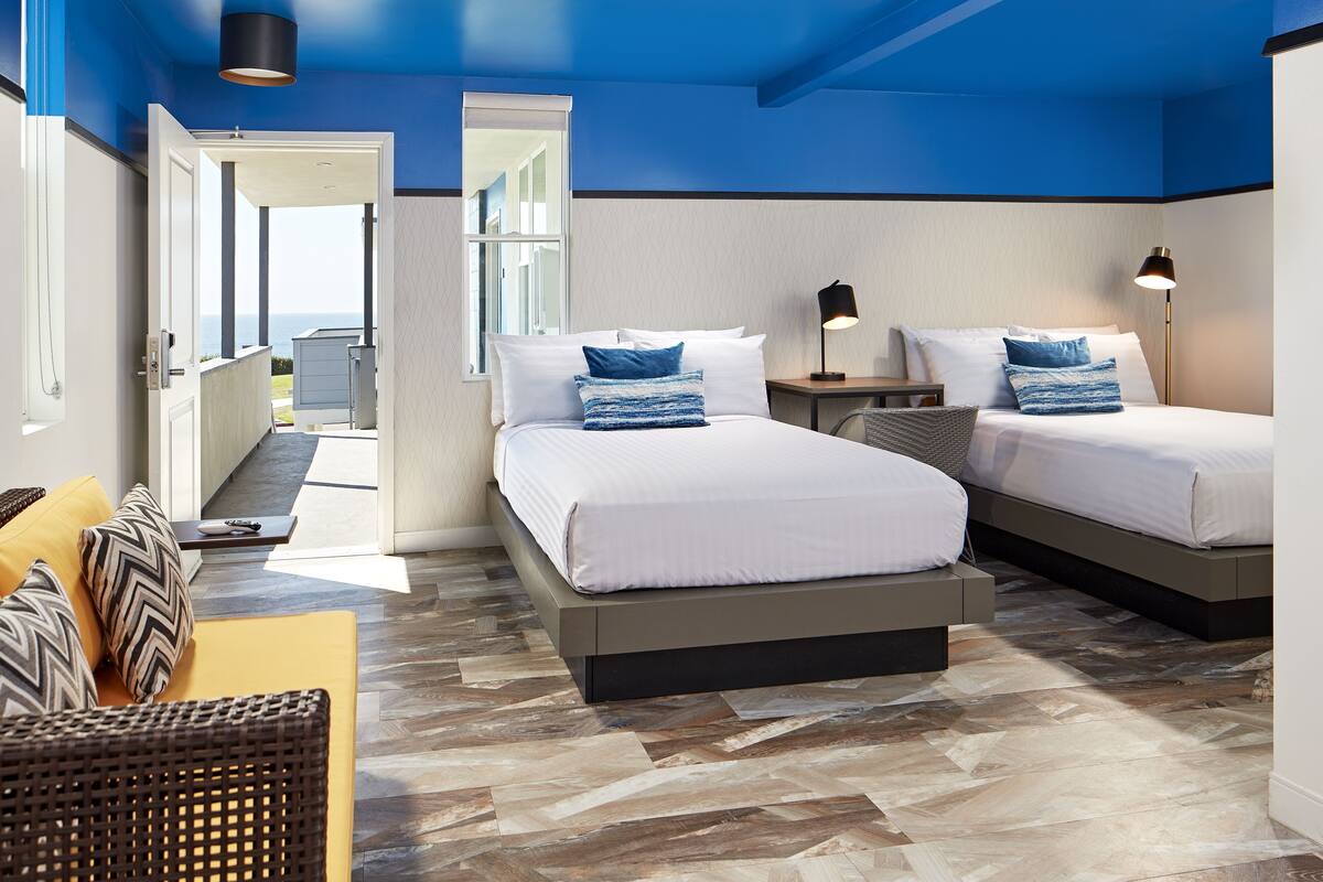 Ett hotellrum med två sängar, en soffa och utsikt över havet.