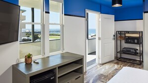 Een moderne hotelkamer met een groot bed, een televisie, een bureau met een computer en uitzicht op de oceaan door de ramen.