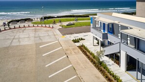 Een parkeerplaats met uitzicht op de oceaan, een gebouw met blauwe accenten, en een voetpad.