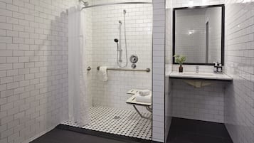 Ein modernes Badezimmer mit weißen Fliesen im U-Bahn-Stil, einer Duschkabine aus Glas, einem spiegeln schwarzen Rahmen und einem kleinen Waschbecken mit einer Pflanze.