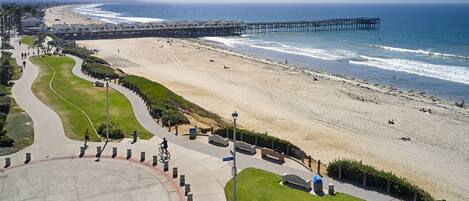 A coastal beach with a pier, a walking path, and a grassy area.