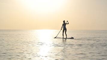 A person paddleboarding on a calm body of water during sunset.