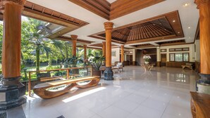 A spacious lobby with high ceilings, wooden columns, and a large glass window overlooking a garden. - Bhuwana Ubud Hotel and Farm (Ubud)