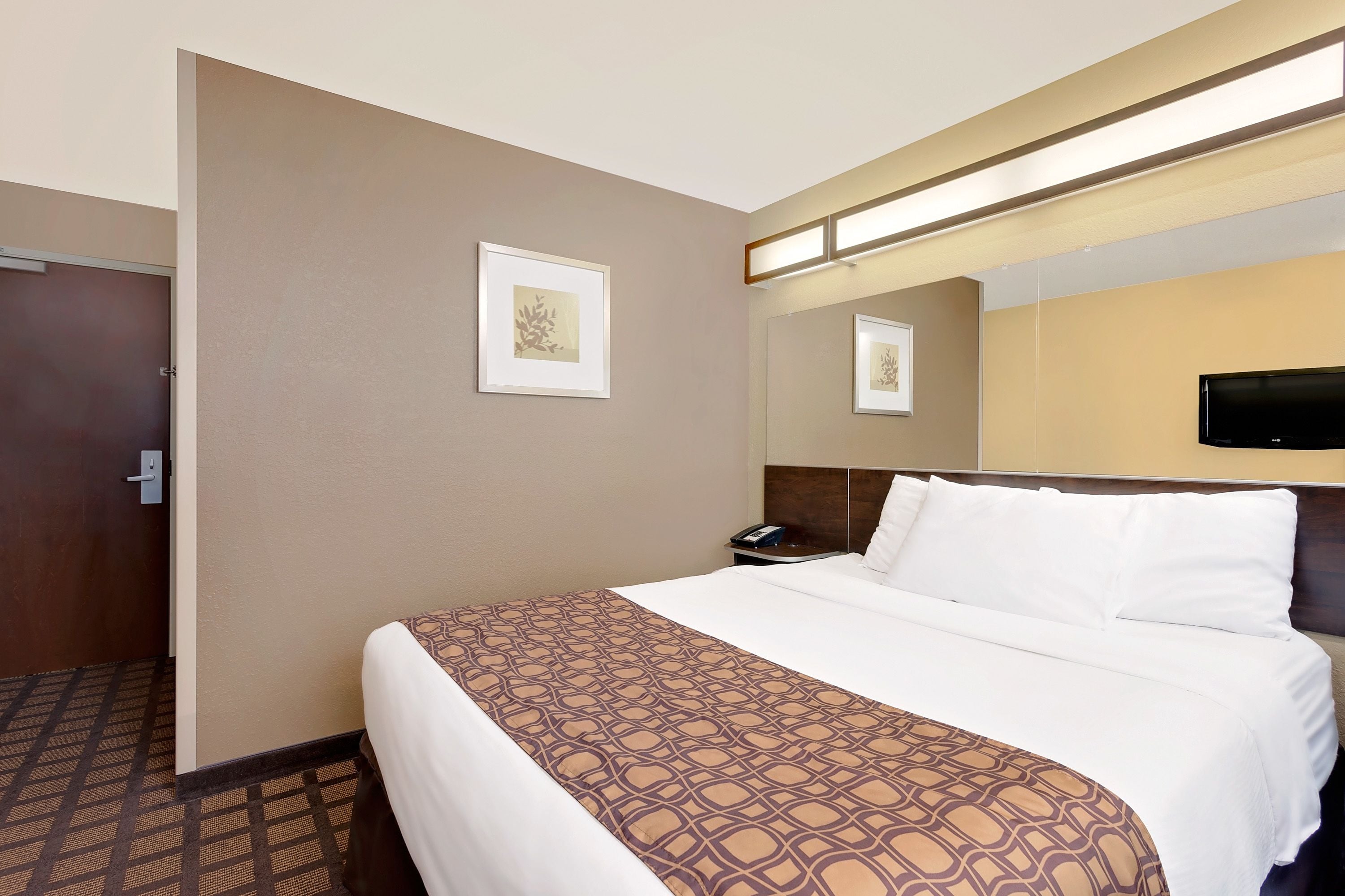 A hotel room with a large bed, a bedside table with a phone, and a wall-mounted TV.