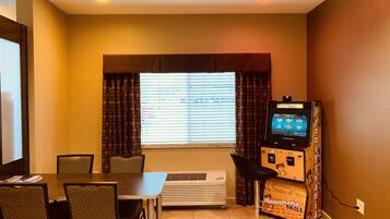 Quarto com mesa, cadeiras, máquina de venda automática e janela com persianas.