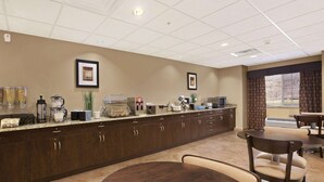 A hotel kitchen with a long counter, various appliances, and framed pictures on the wall.