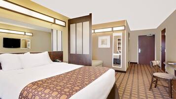 A hotel room with a large bed, a desk, a chair, a television, and a mirror.