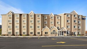 A multi-story hotel with a central entrance, a parking lot, and a clear sky.