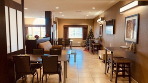 A hotel dining area with multiple tables and chairs, a Christmas tree, and a large window with curtains.