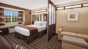 A hotel room with a bed, a sofa, a window with curtains, a picture on the wall, and a patterned carpet.