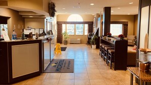 A hotel lobby with a reception desk, seating area, and a large window providing natural light.