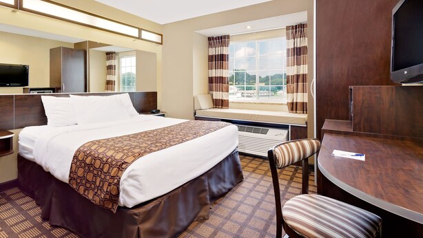 A hotel room with a bed, a desk, a chair, a TV, and a large window with curtains.