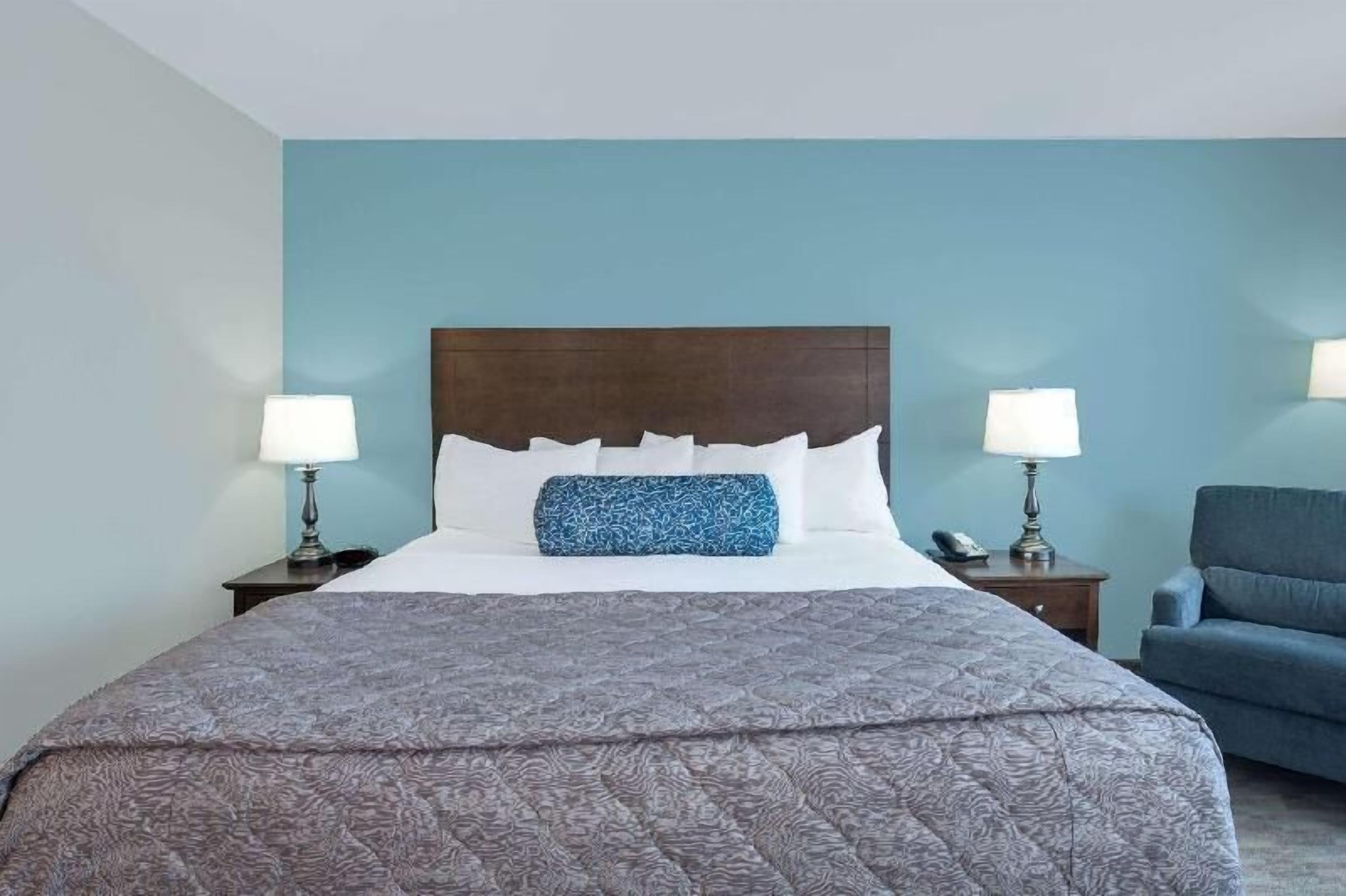 Une chambre d’hôtel avec un grand lit, deux tables de chevet, une chaise bleue et une tête de lit en bois.