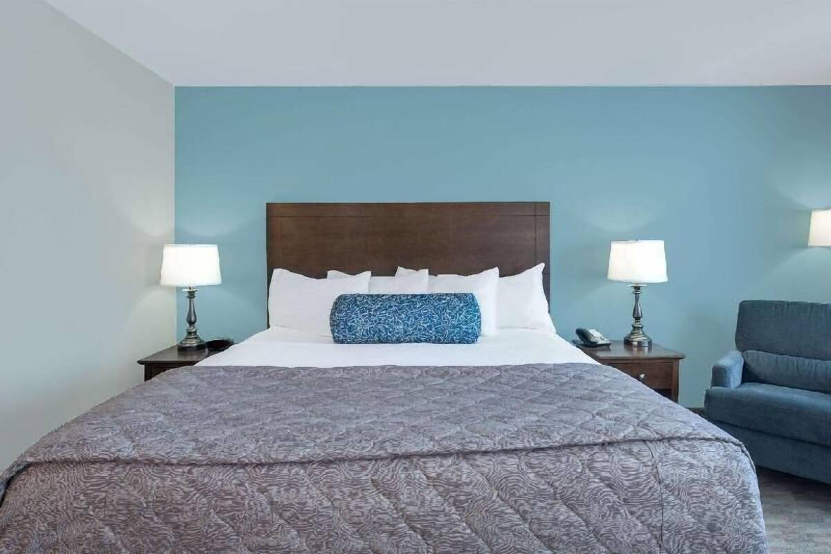 Een hotelkamer met een groot bed, twee nachtkastjes, een blauwe stoel en een houten hoofdbord.