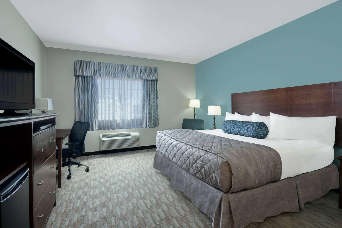 Een hotelkamer met een bed, bureau, stoel, televisie en airconditioning.