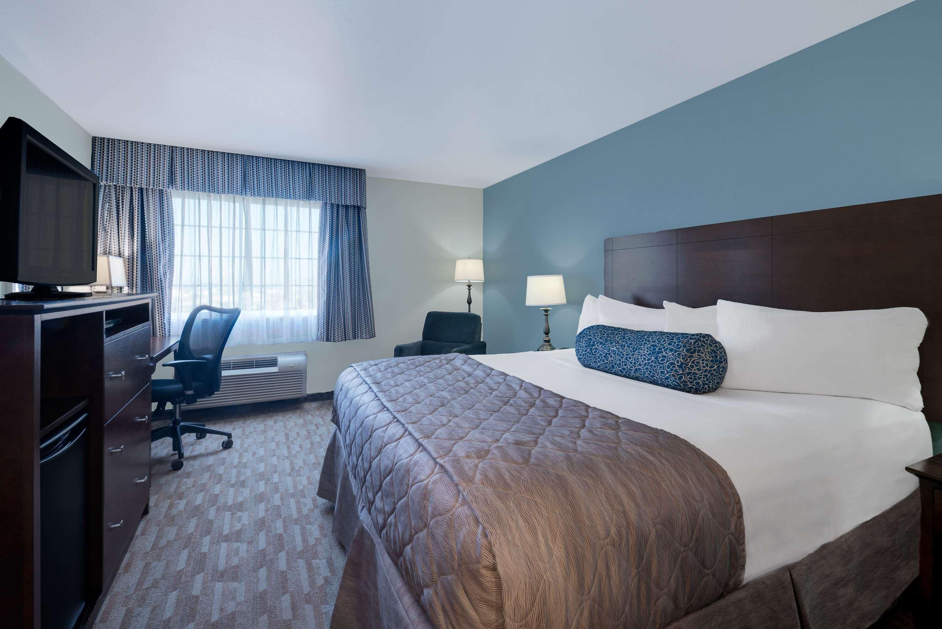 Une chambre d’hôtel équipée d’un lit, d’un bureau, d’une télévision, d’une chaise et d’une fenêtre avec des rideaux.
