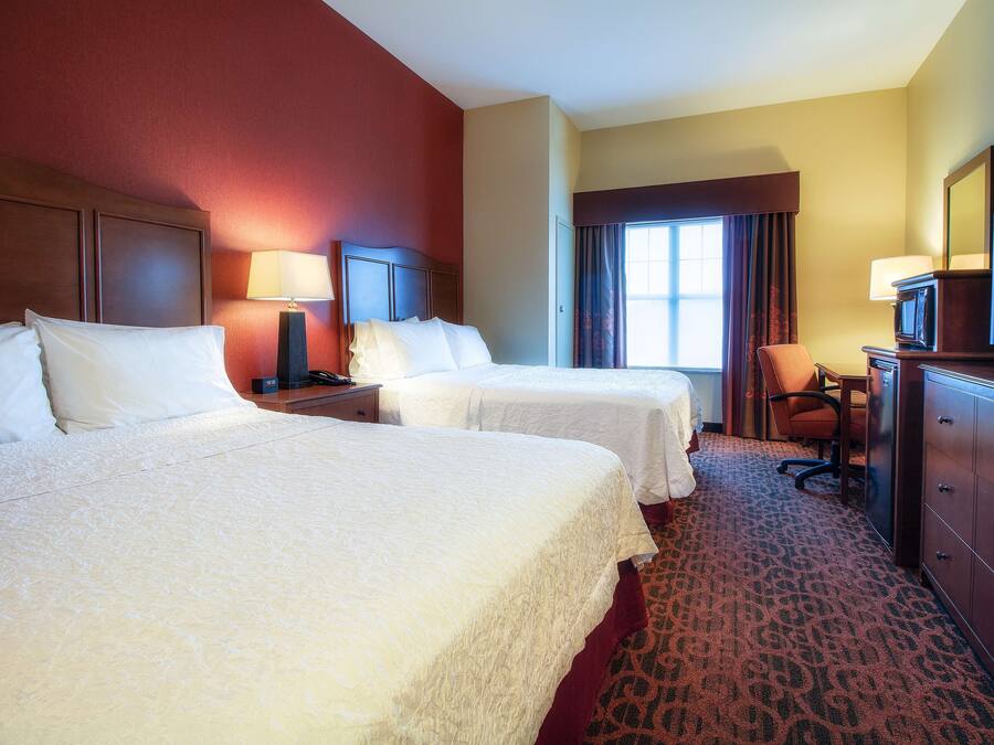 A hotel room with two beds, a desk, a chair, a TV, and a dresser.