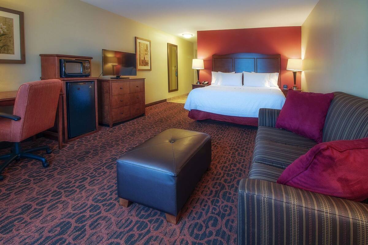 A hotel room with a bed, a desk with a computer, a chair, a couch, and a small table.