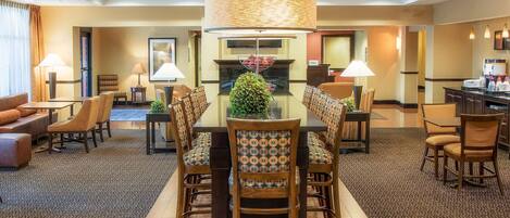 A hotel dining area with a large table, multiple chairs, a chandelier, and a fireplace.
