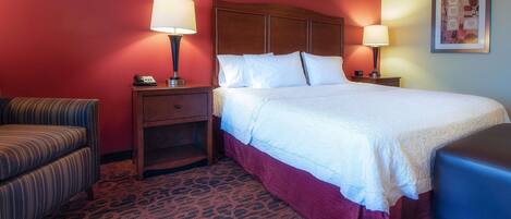 A hotel room with a large bed, two bedside tables with lamps, a chair, and a patterned carpet.
