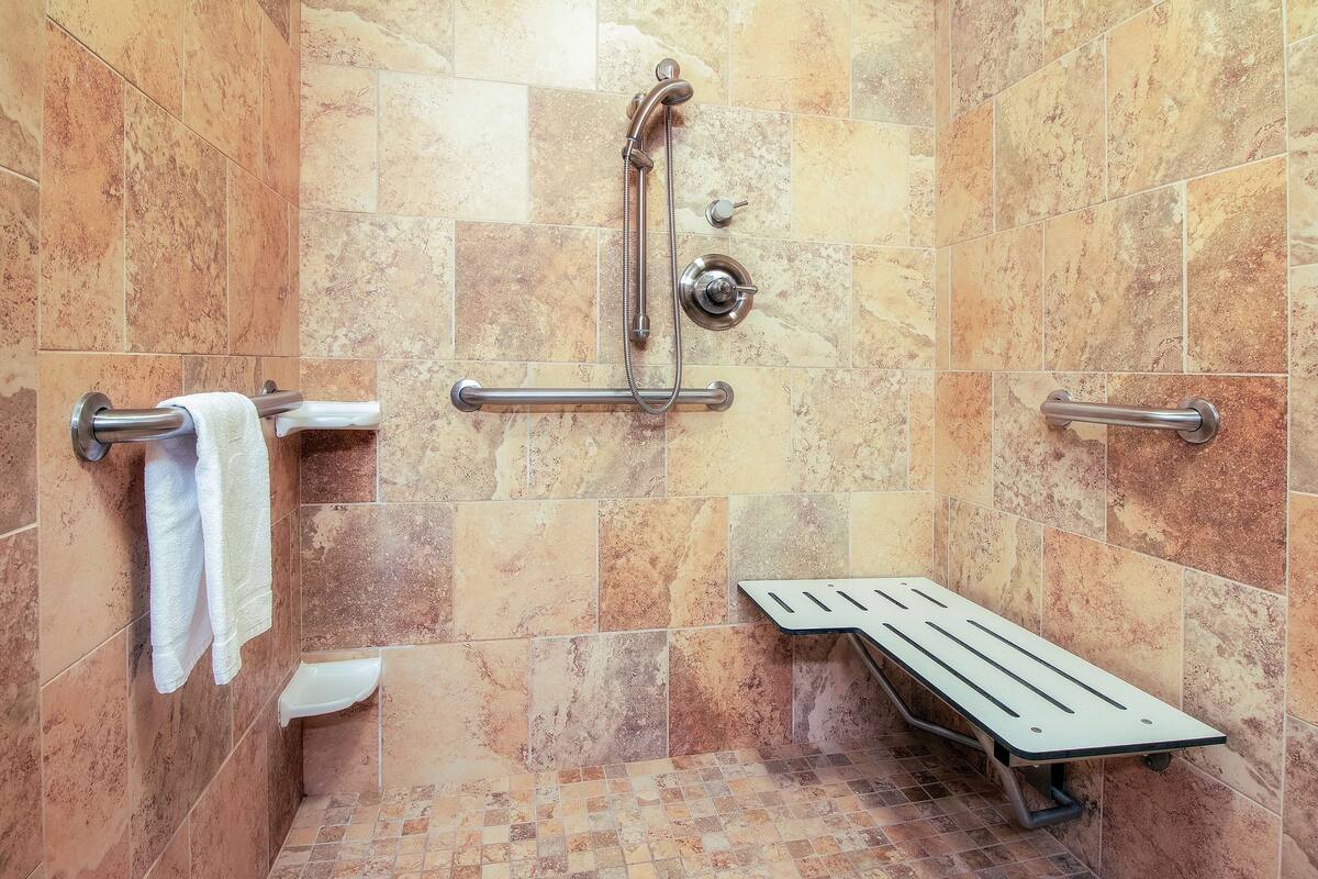 A shower with a handheld showerhead, grab bars, and a bench.