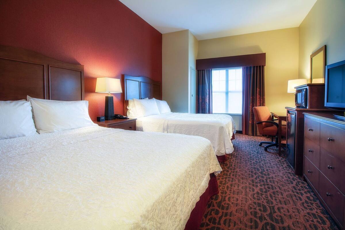 A hotel room with two beds, a desk, a chair, a dresser, and a television.