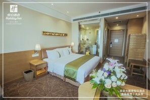 A hotel room with a large bed, bedside tables, a mirror, a wooden headboard, a small table with a vase of flowers, and a door leading to a bathroom. - Holiday Inn Xi'an Big Goose Pagoda by IHG (Xi'an)