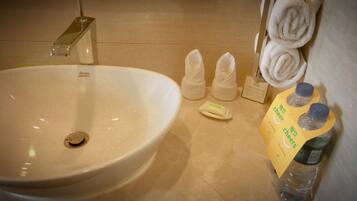 A bathroom with a large sink, towels, toiletries, and a water bottle.