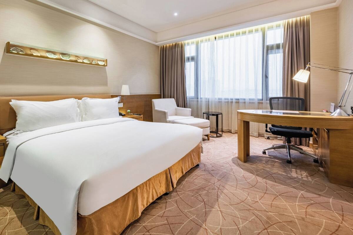 A hotel room with a large bed, a desk, a chair, and a small table.