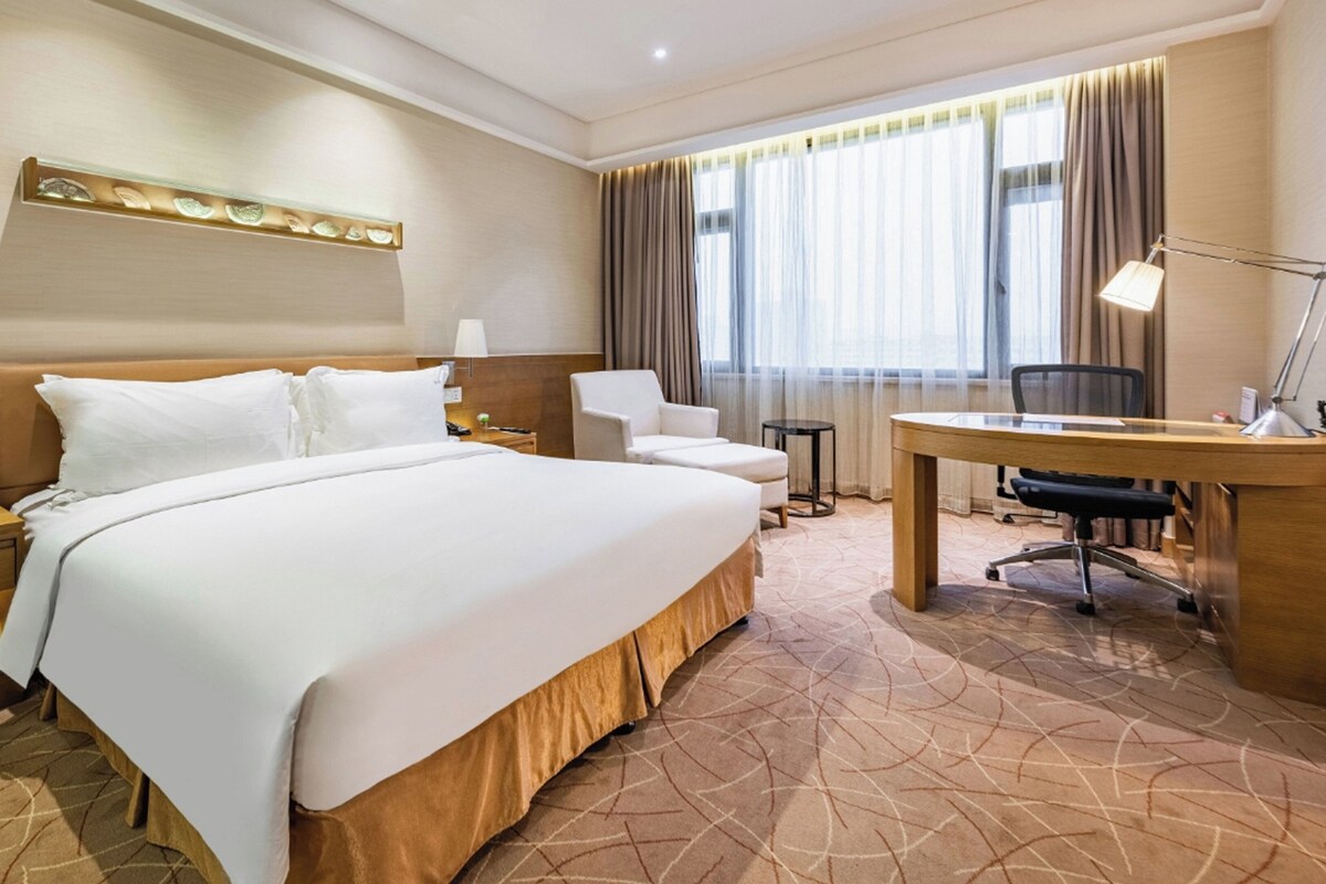 A hotel room with a large bed, a desk, a chair, and a small table.