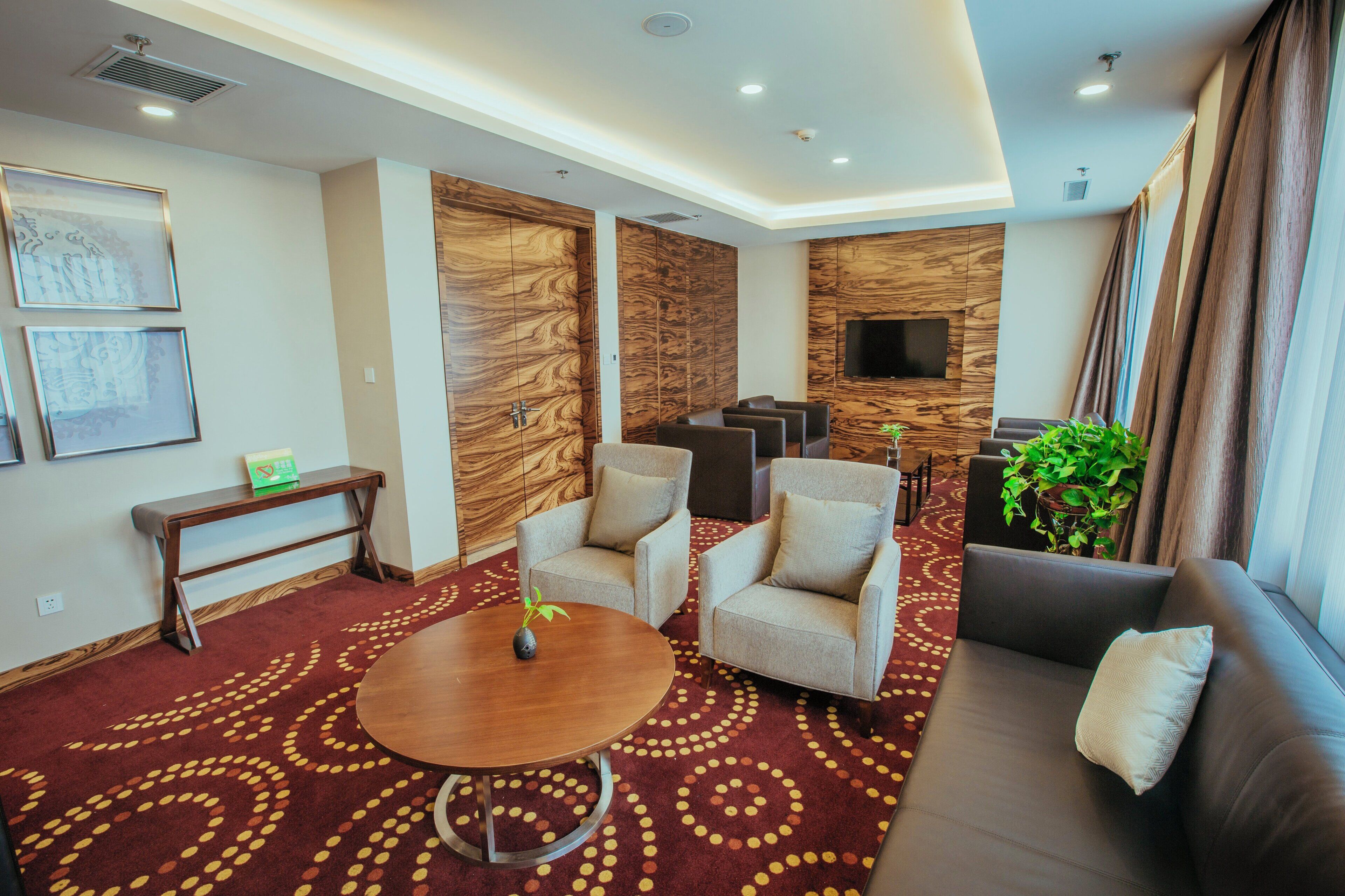Un hall d’hôtel avec un canapé, des fauteuils, une petite table et un téléviseur fixé à un mur en bois.