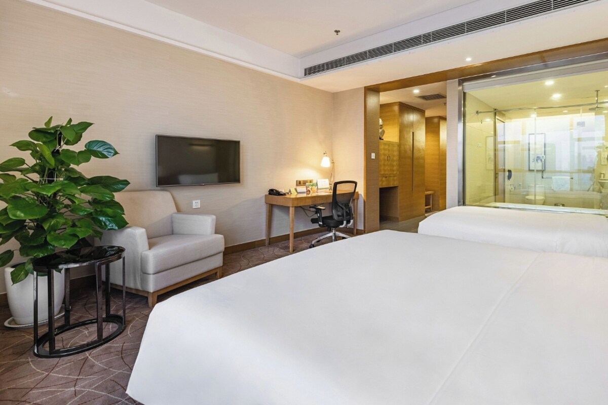 A hotel room with a large bed, a desk with a chair, a television, and a potted plant.