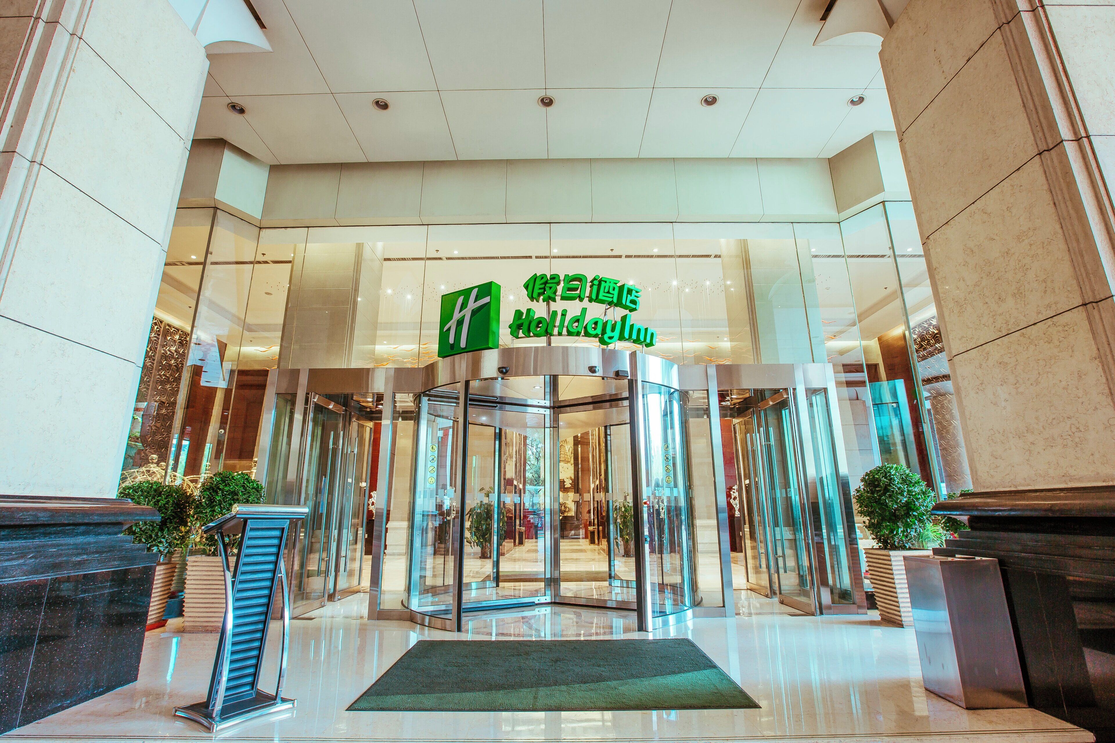 A hotel entrance with a revolving door, glass walls, and a green sign above.