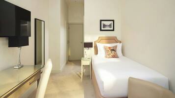 A hotel room with a bed, a desk, a chair, a TV, and a bedside table with a lamp.