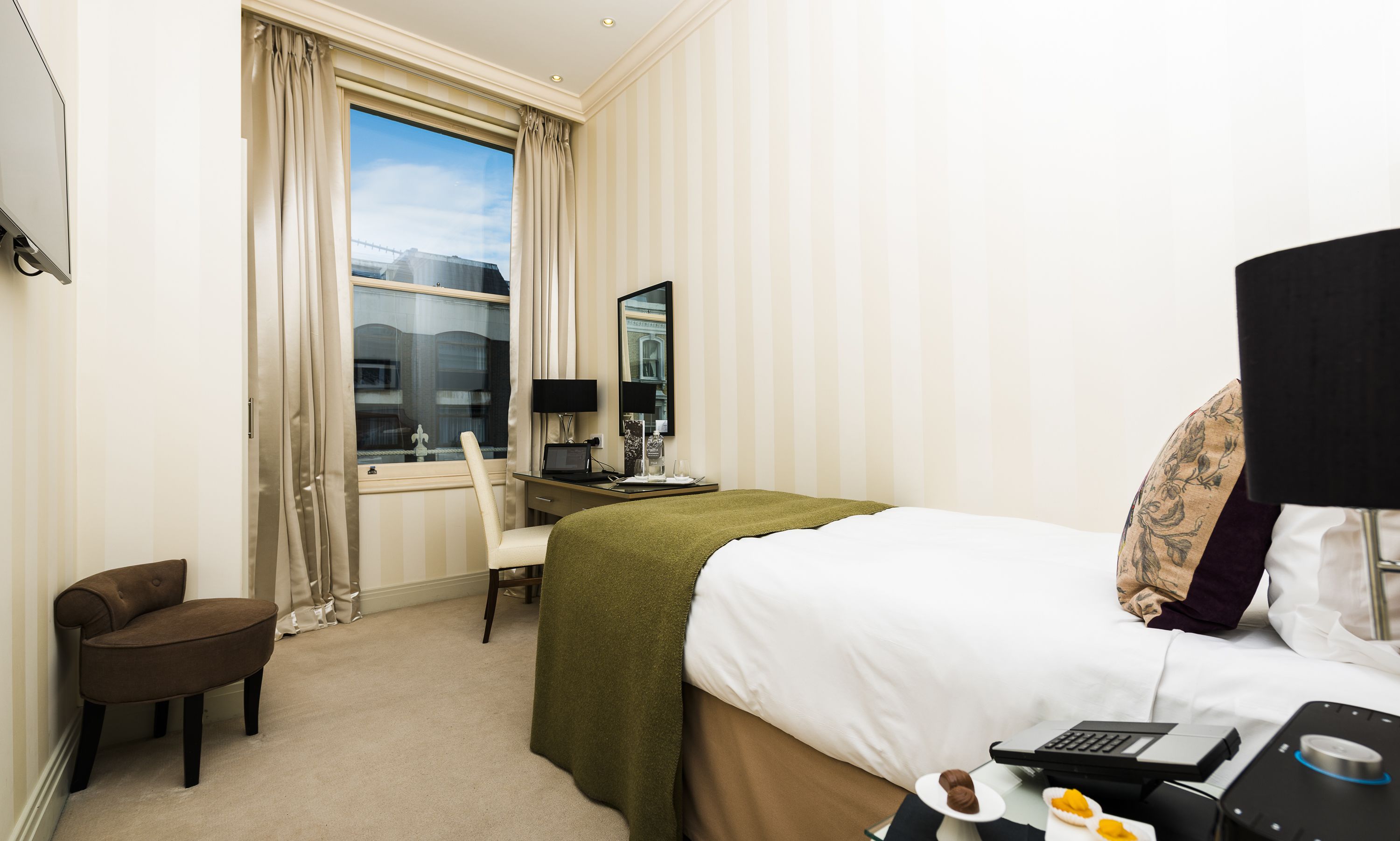 A hotel room with a bed, a desk with a computer, a chair, a window with curtains, and a view of a bridge.