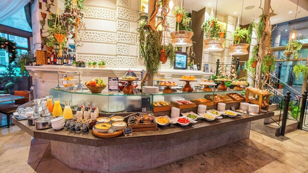 Un buffet proposant une variété de plats et de boissons, un comptoir vitré, des plantes suspendues et un mur décoratif.
