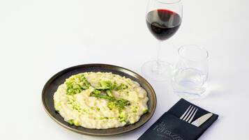 A plate of creamy risotto garnished with green herbs, a glass of red wine, and a folded napkin with a fork and knife on a white background.