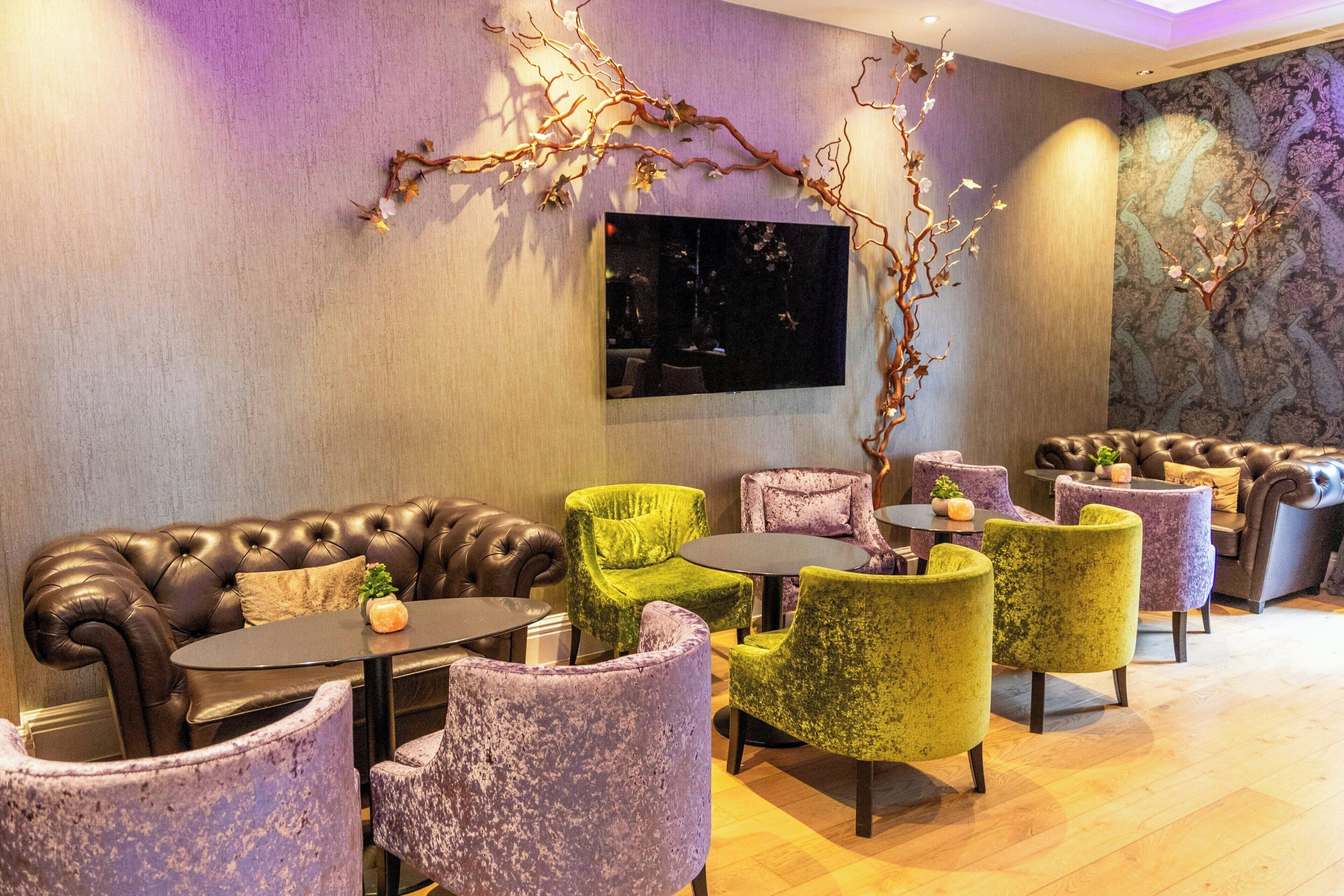 A lounge area with leather sofas, green and purple armchairs, and a large wall-mounted TV.