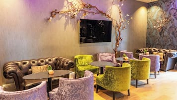 A lounge area with leather sofas, green and purple armchairs, and a large wall-mounted TV.