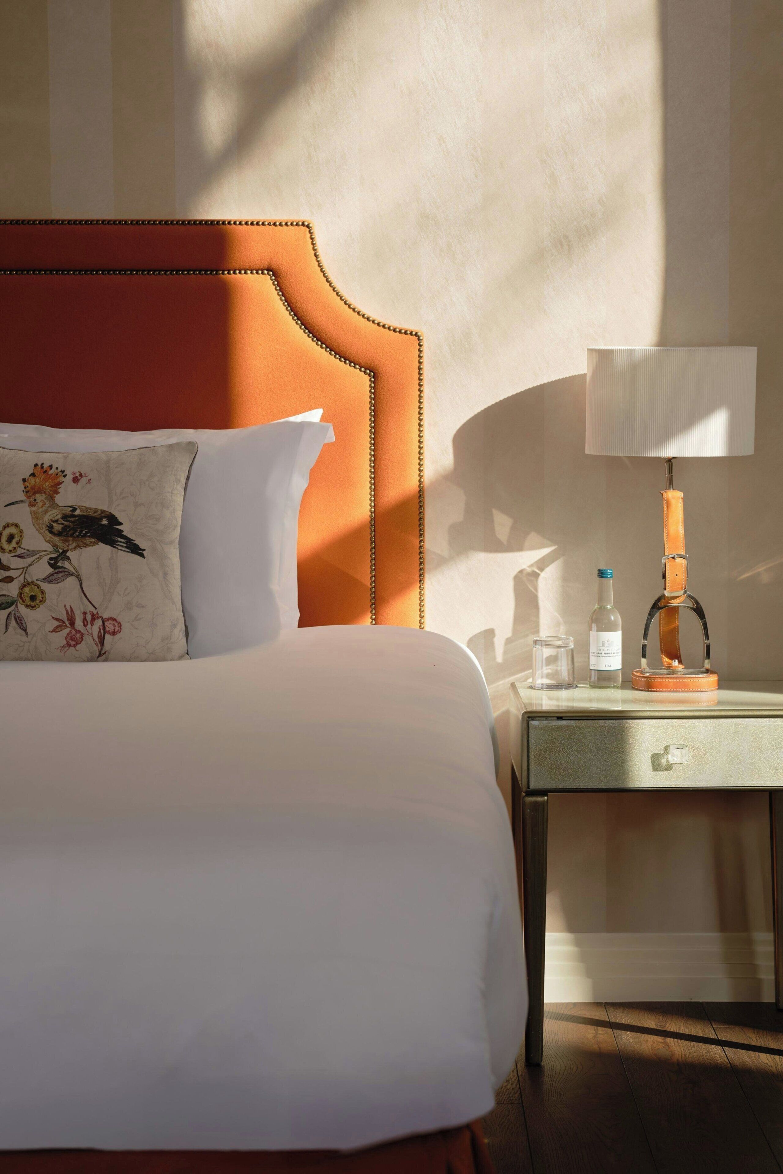A hotel room with a bed, a nightstand, a lamp, and a bottle of water.