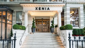 Une entrée imposante avec un escalier menant à une porte portant l’inscription « XENIA ».